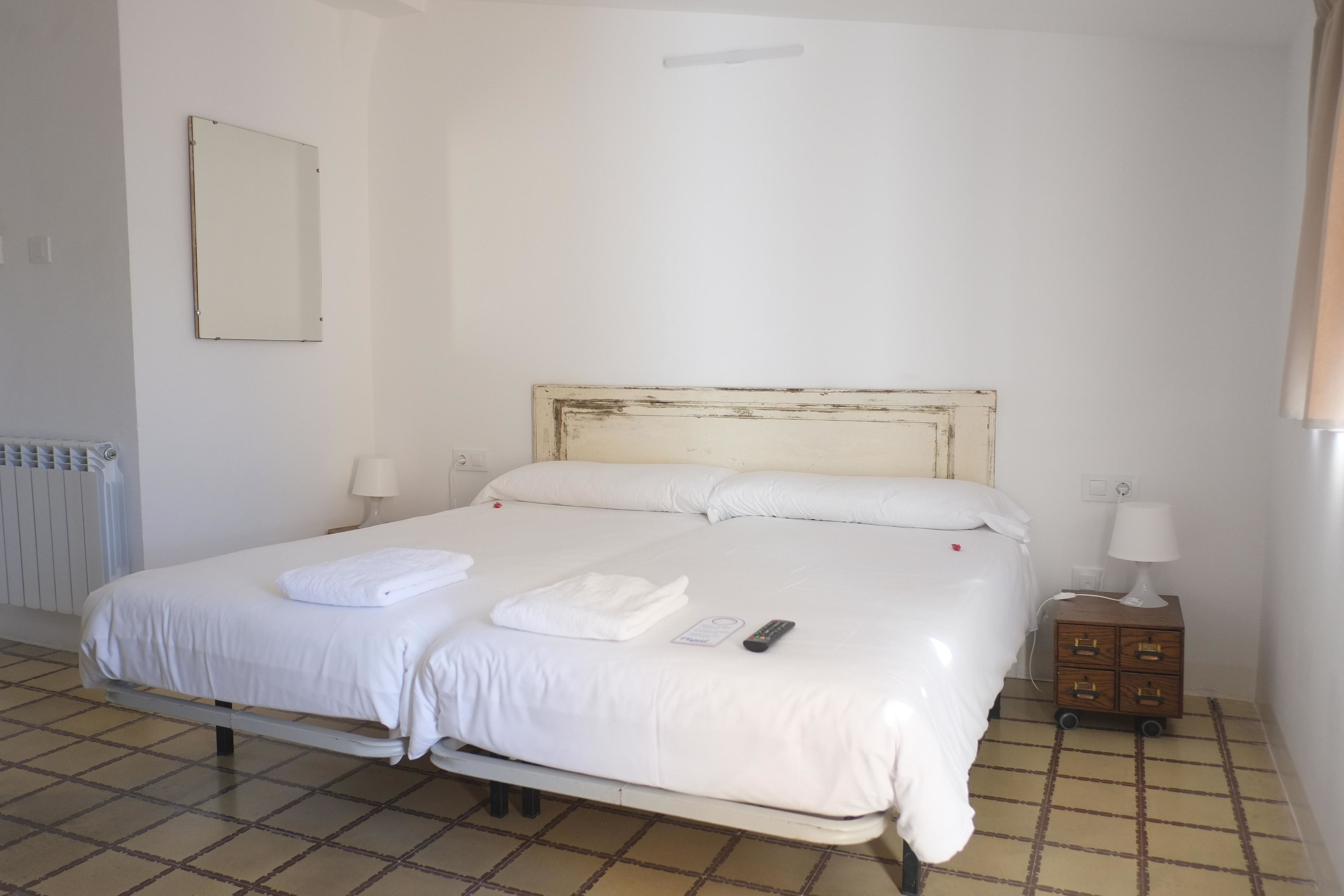 Una cama bien hecha con sábanas blancas, una mesita de noche con una lámpara y un pequeño armario de madera.