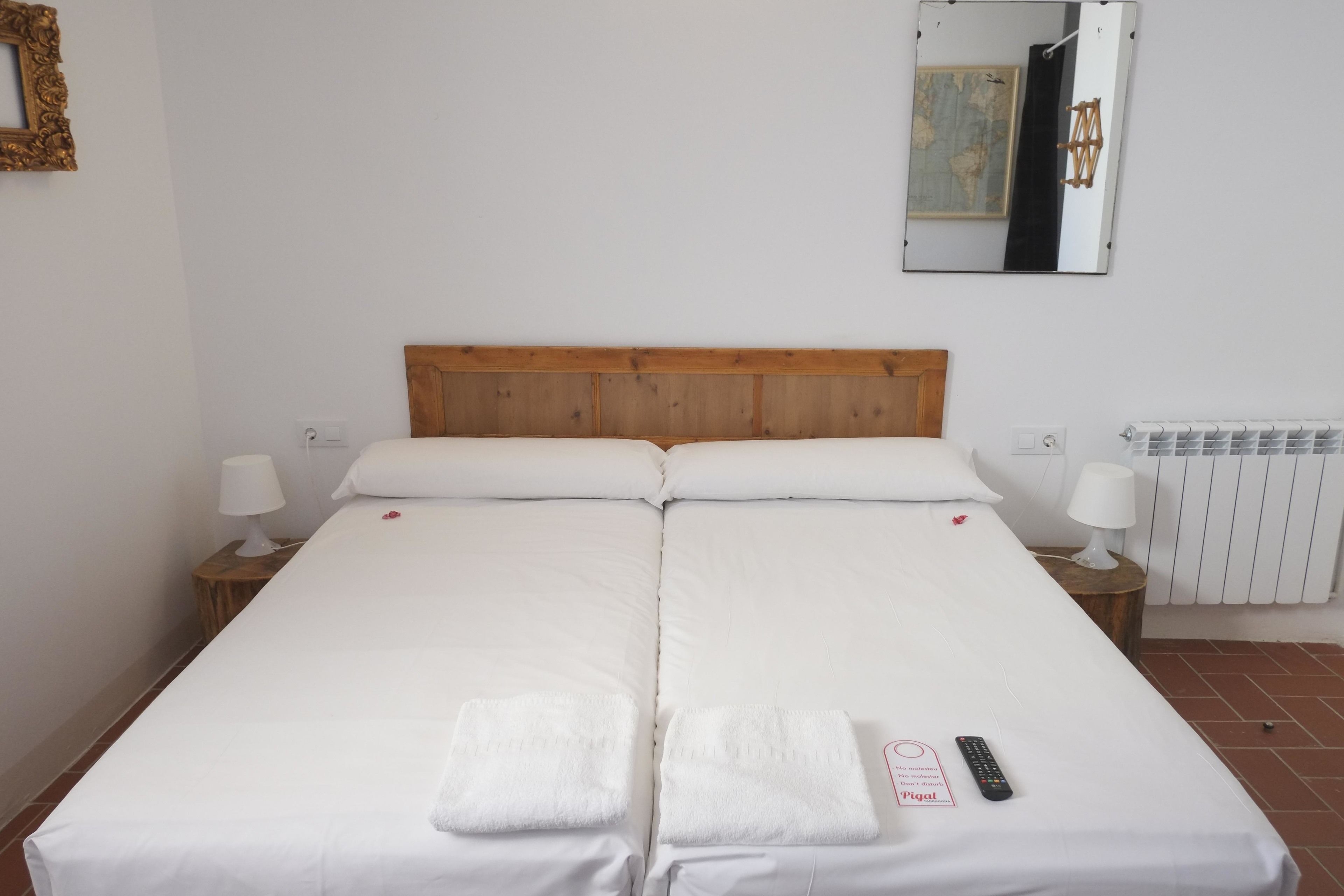 Un lit double avec du linge de lit blanc, deux tables de chevet avec des lampes, un miroir au mur et un radiateur.
