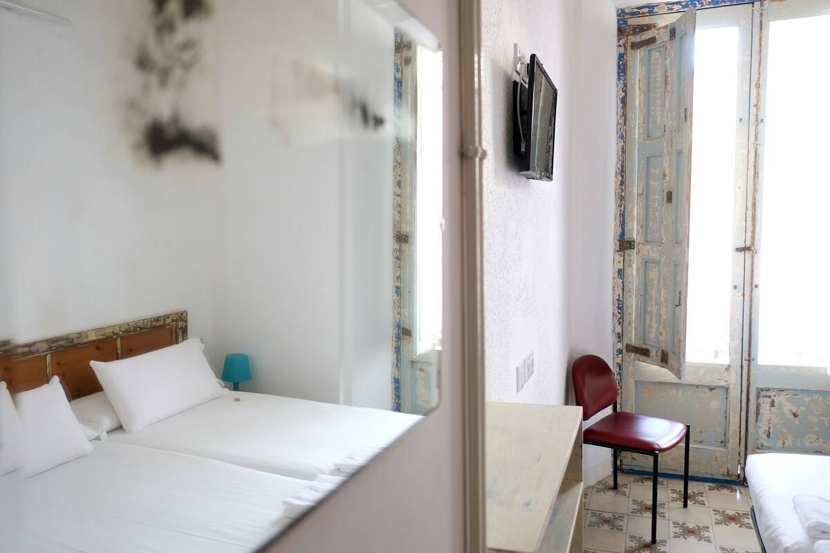 Una habitación con cama, sillón, televisor y ventana.