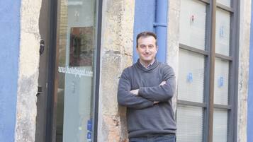 Un homme se tient devant un bâtiment dont la porte est en verre et sur laquelle est affichée l’adresse d’un site web.