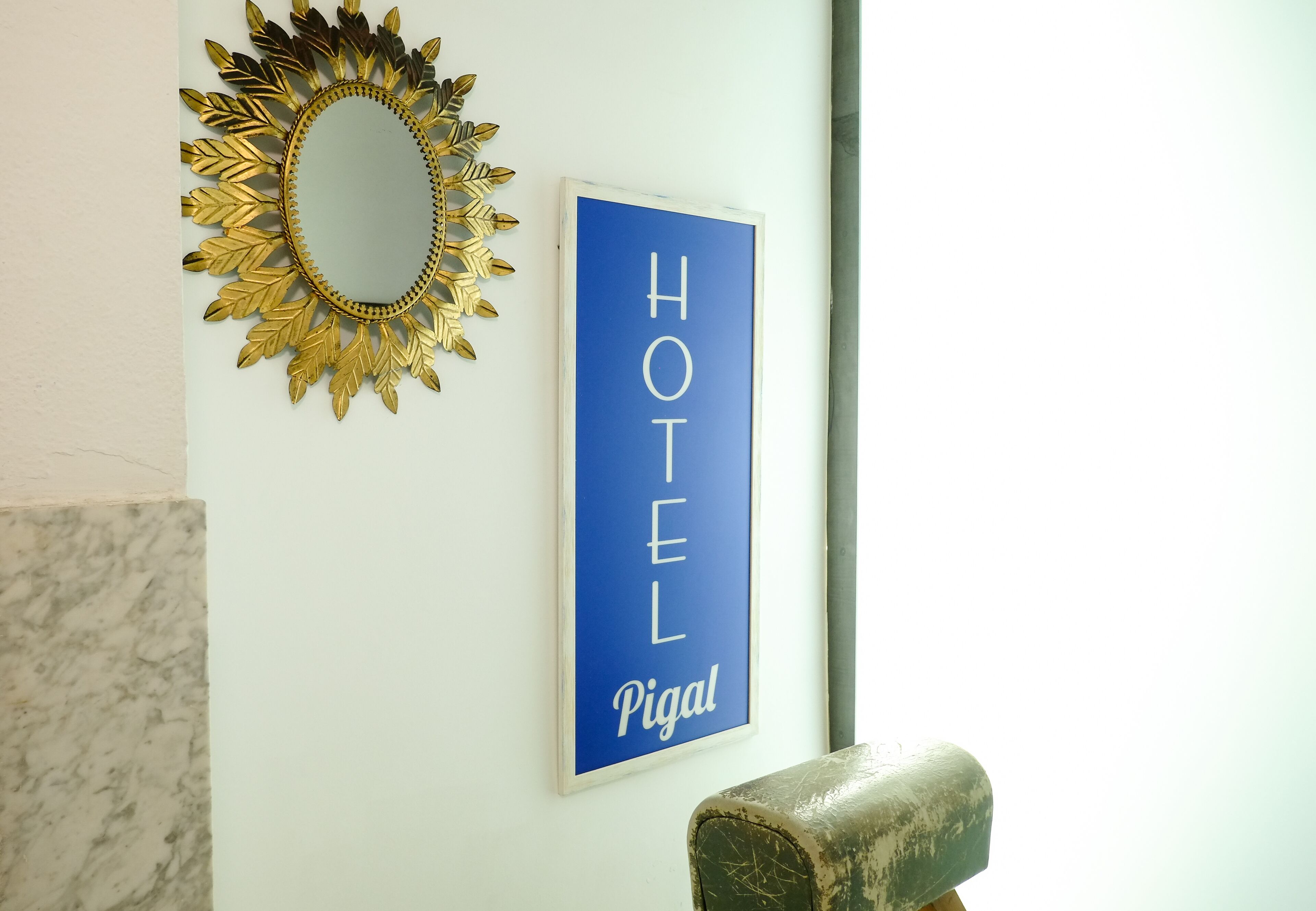 Eine Wand mit einem goldfarbenen Spiegel und einem blauen Schild mit der Aufschrift 'HOTEL Pigal'.