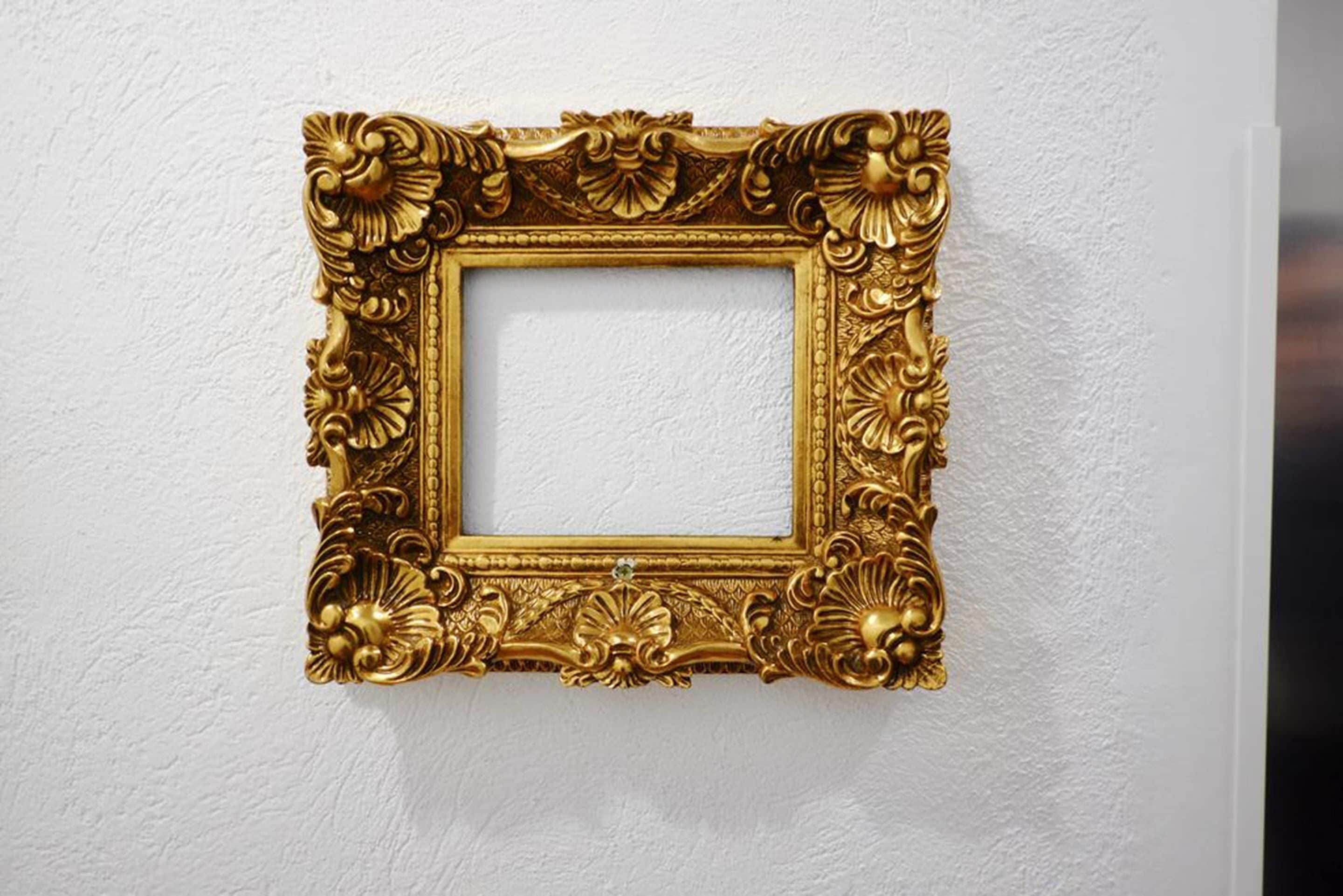 A gold-framed picture hanging on a textured white wall.