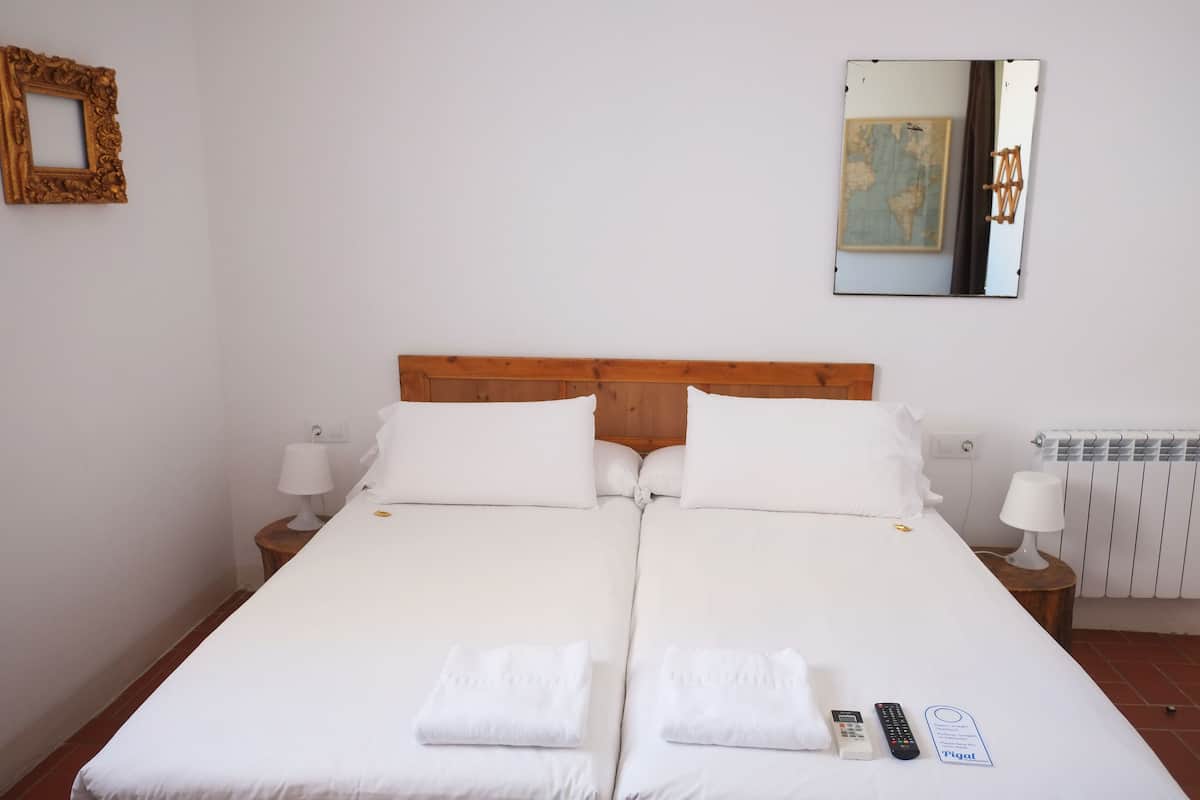 Una cama doble con ropa de cama blanca, dos mesitas de noche con lámparas, un cuadro en la pared y un mapa.