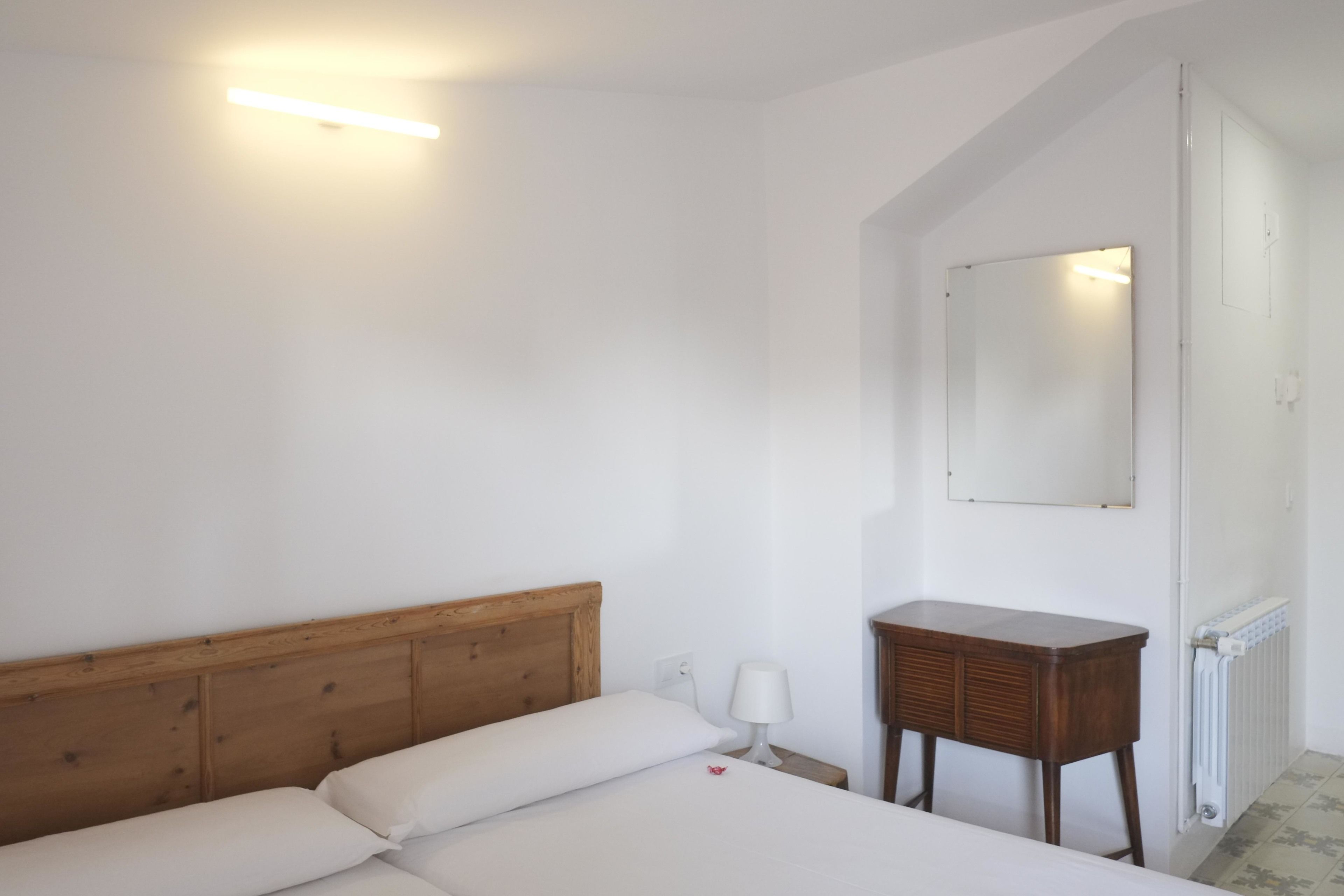 Quarto com cabeceira de madeira, mesa de cabeceira com abajur e espelho na parede.