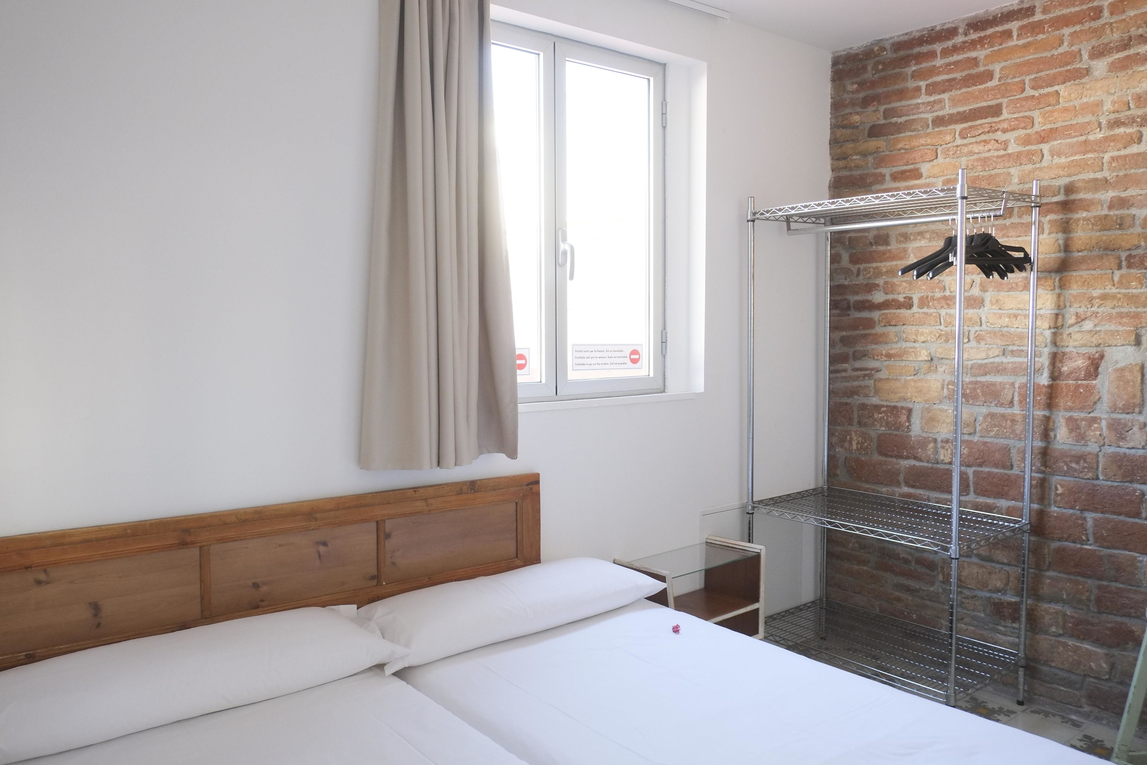 Habitación de hotel con una cama de cabecera de madera, una estantería metálica y una pared de ladrillo.