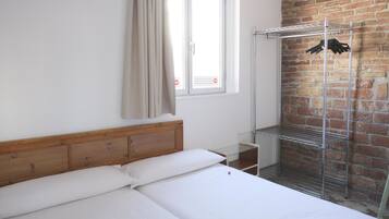 Habitación de hotel con una cama de cabecera de madera, una estantería metálica y una pared de ladrillo.