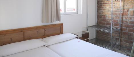 A hotel room with a wooden headboard bed, a metal shelf unit, and a brick wall.
