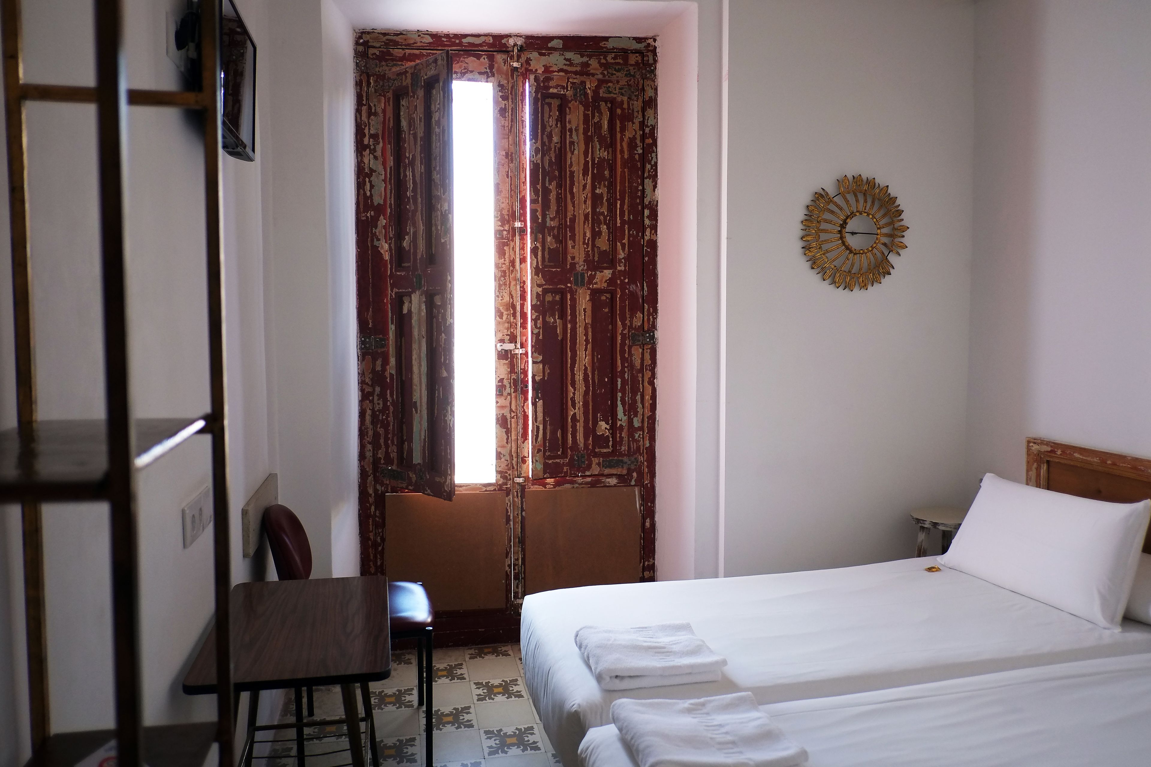 A bedroom with a bed, a chair, a desk, and a door with a decorative mirror.
