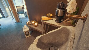 Un lavamanos de piedra con un grifo moderno, velas y una cafetera sobre un alféizar de piedra.