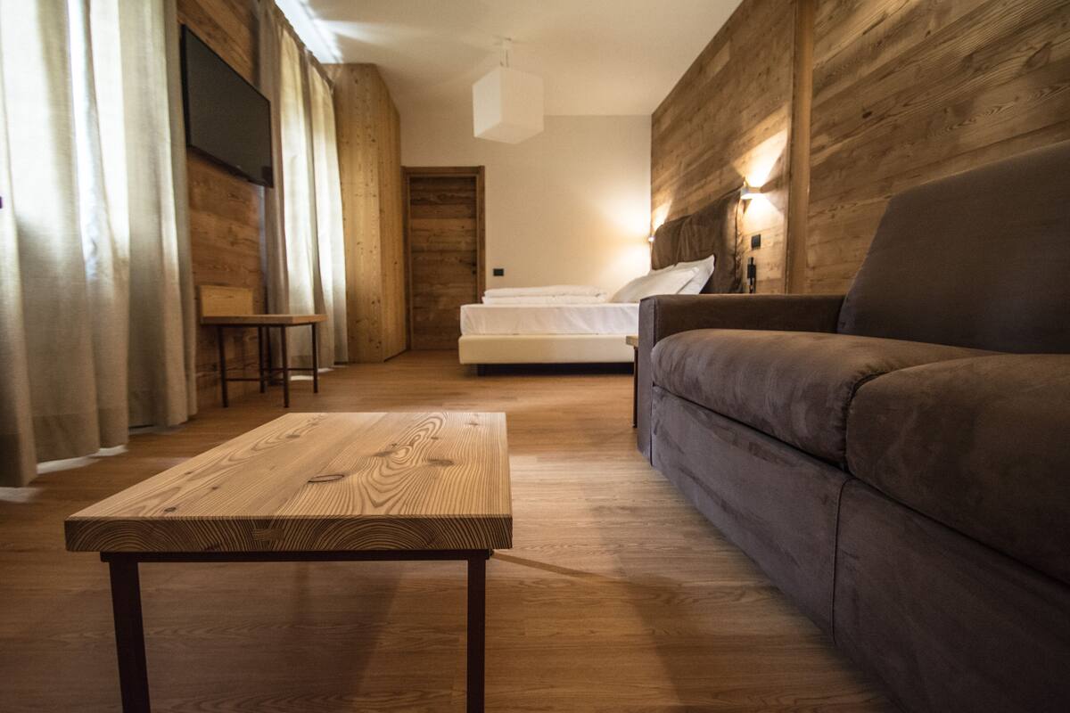 A wooden-floored room with a sofa, a wooden table, and a bed with white bedding.