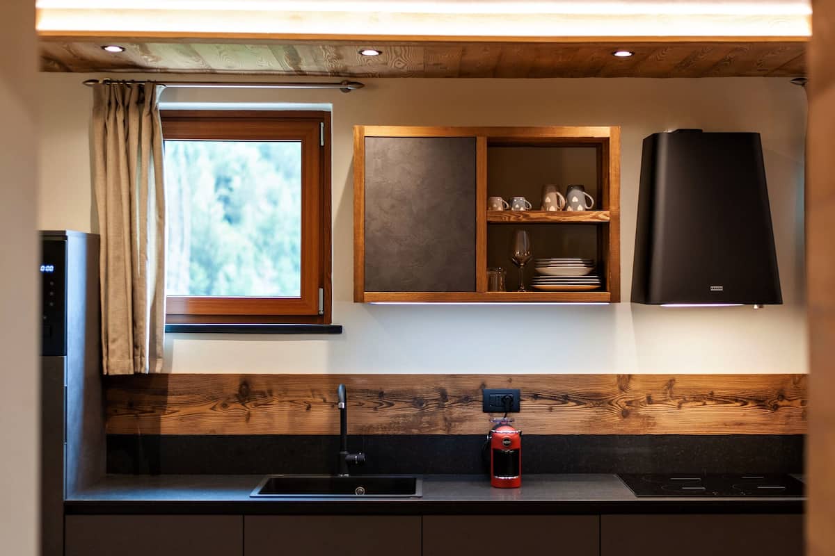 A modern kitchen with a built-in oven, a coffee machine, and a window with curtains.