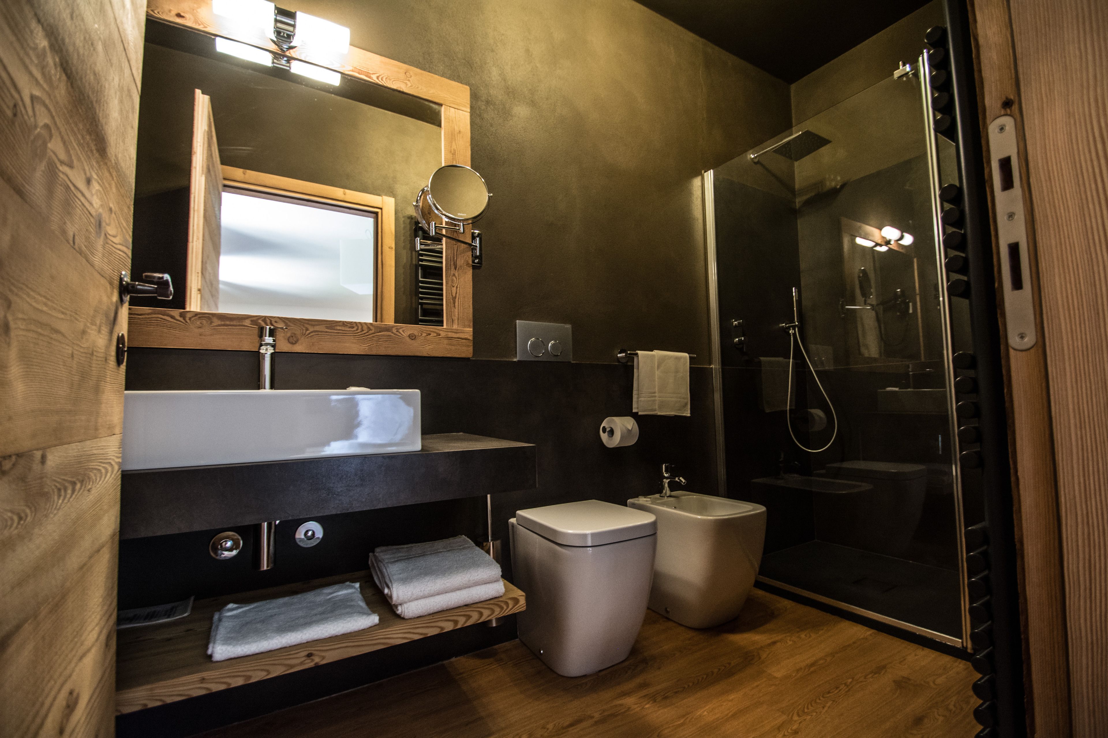 A modern bathroom with a wooden vanity, a large mirror, a built-in sink, a shower, and two trash bins.