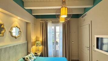 A hotel room with a bed, a TV, a lamp, and a door leading to a balcony.