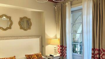 Habitación de hotel con una cama grande, dos lámparas de pared, una mesita de noche con lámpara, un espejo y una ventana con cortinas.