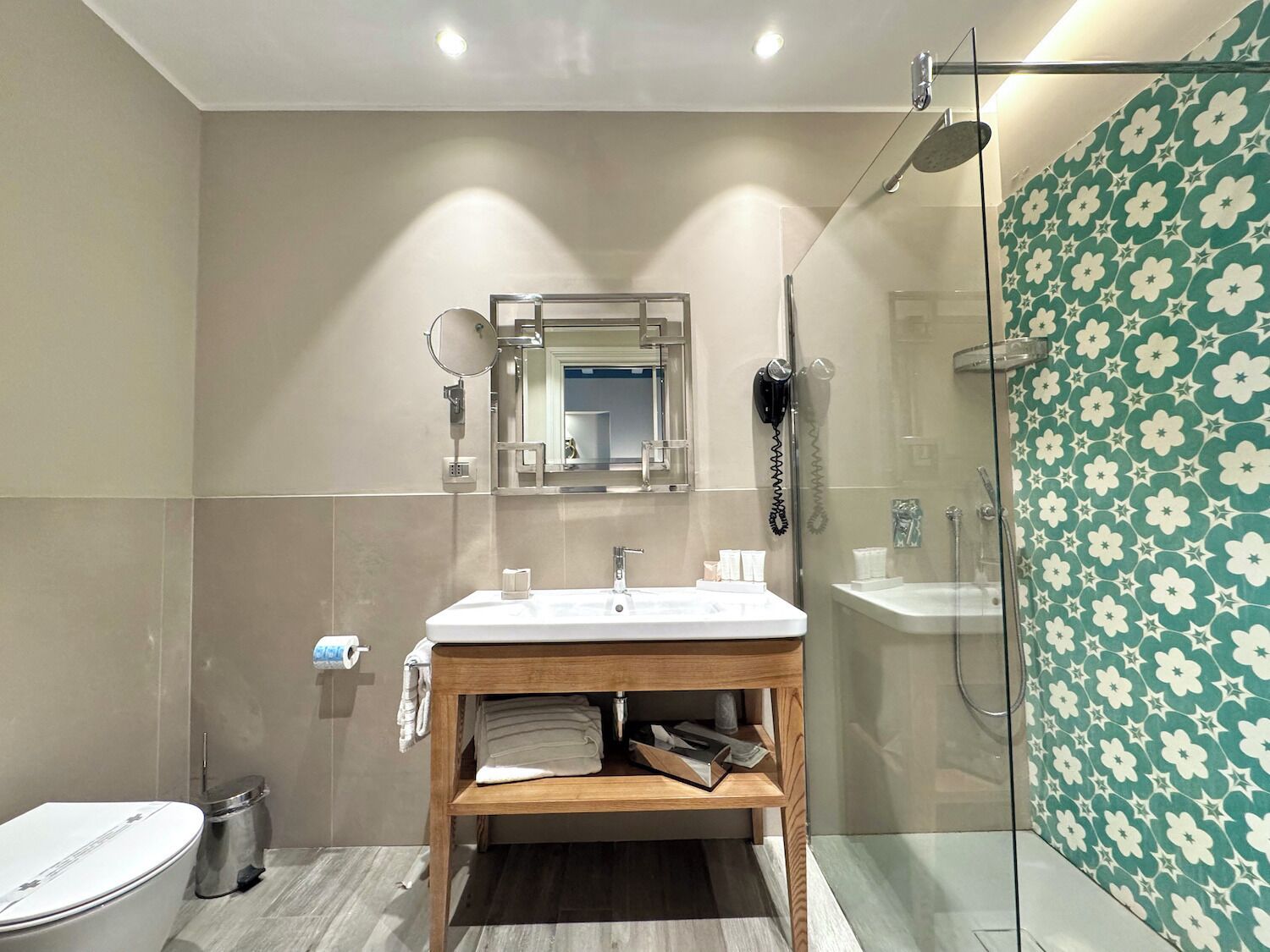 A modern bathroom with a wooden vanity, a large mirror, a hairdryer, and a shower with a glass door.