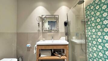 Une salle de bain moderne avec un meuble-lavabo en bois, un grand miroir, un sèche-cheveux et une douche dotée d’une porte en verre.
