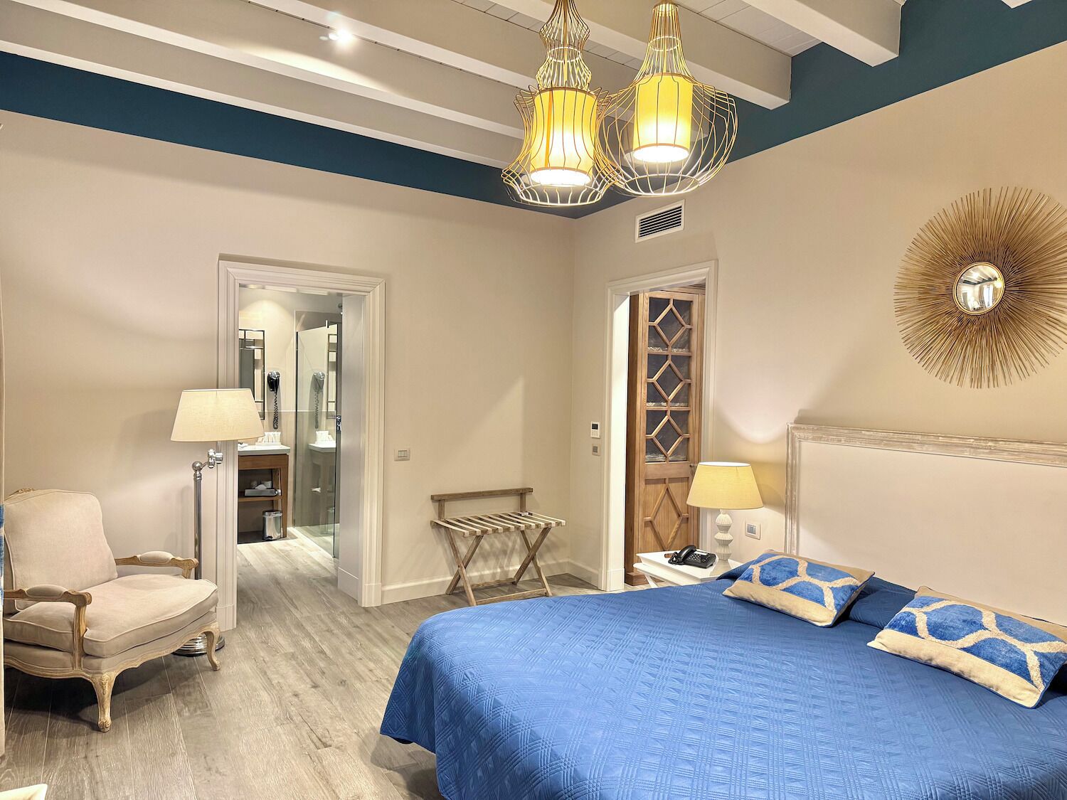A bedroom with a large bed, a chair, a desk, and a mirror.