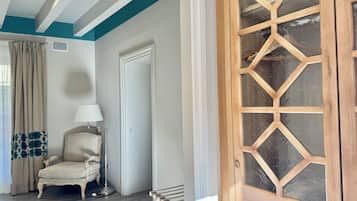 Una habitación con puerta de madera, una silla, una lámpara y un ventanal con cortinas.