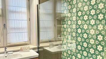 A modern bathroom with a glass-enclosed shower, a vanity with a mirror, and a window with sheer curtains.