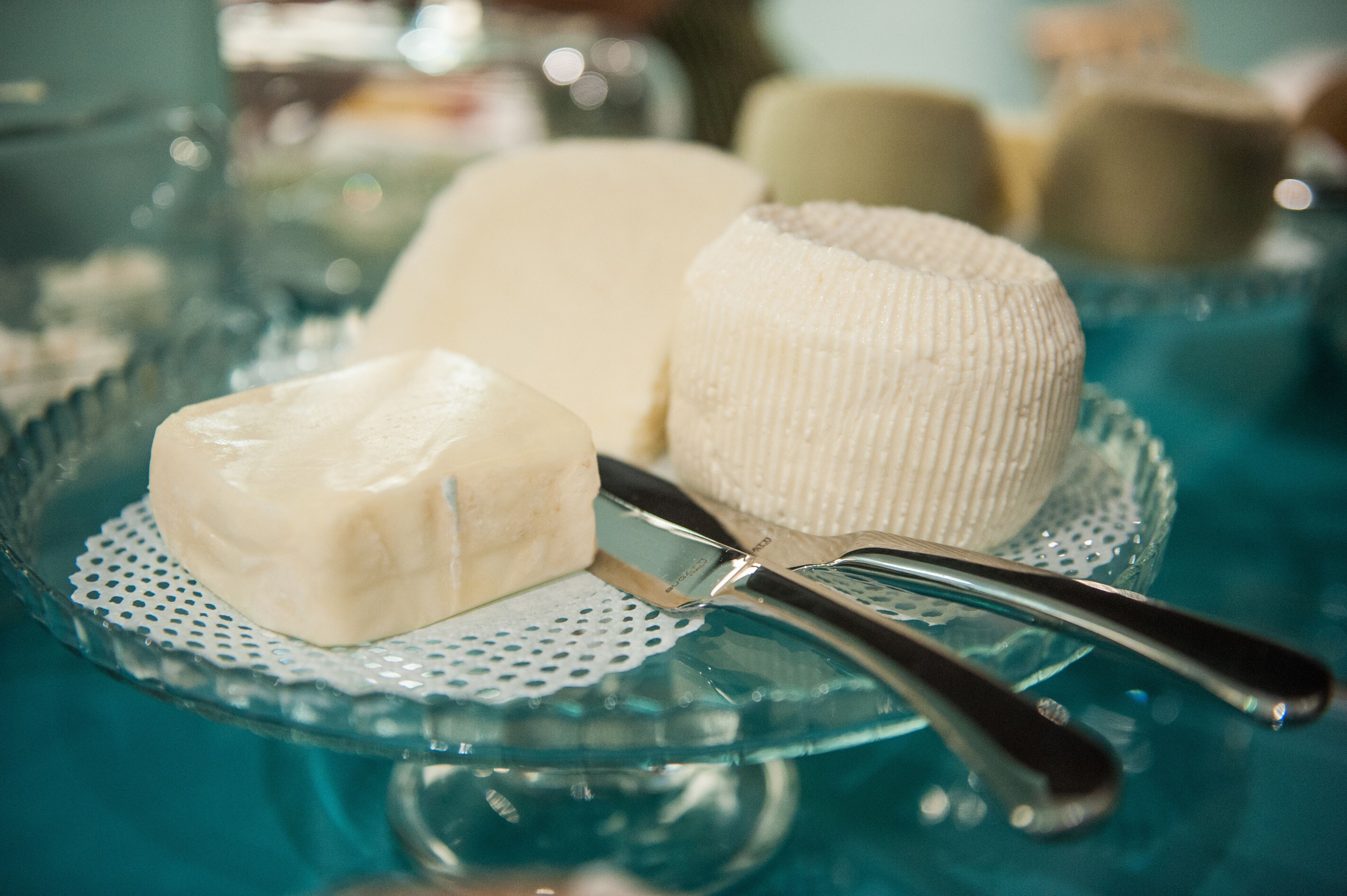 Una losa de vidrio con tres ruedas de queso blanco y un cuchillo para queso.