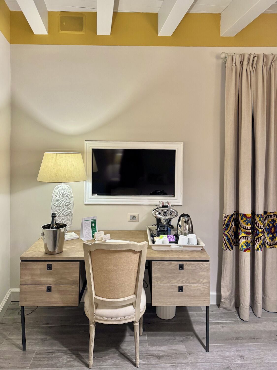 Une chambre d’hôtel équipée d’un bureau, d’une chaise, d’une télévision, d’une lampe, d’une machine à café et d’une bouteille de champagne.
