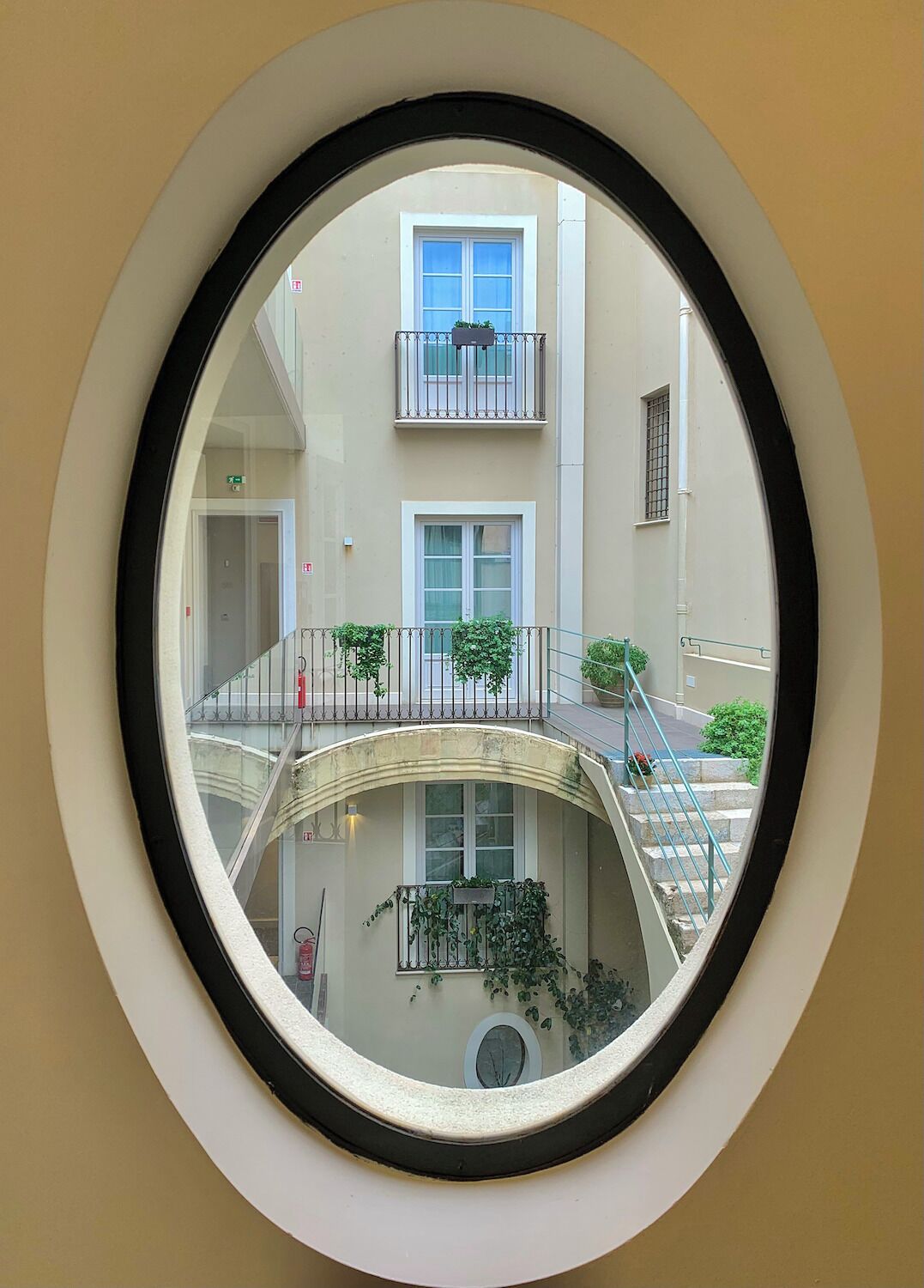 Una ventana circular con vista al interior de un edificio, que incluye una escalera, balcones y ventanas.