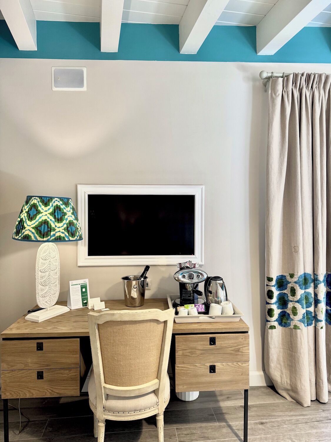 A bedroom with a bed, a desk with a computer, a lamp, and a window with curtains.