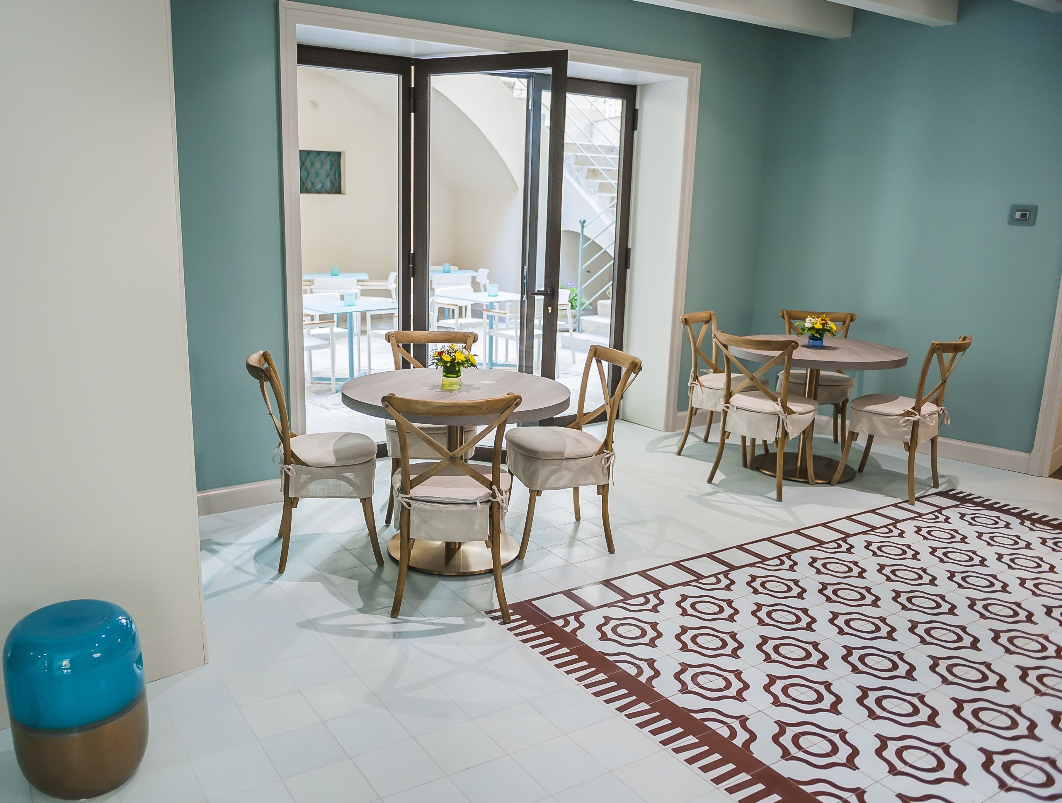 A dining area with round tables and chairs, a patterned floor, and a view through a glass door to an outdoor seating area.