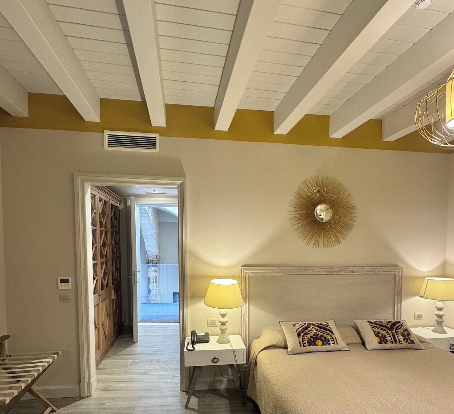 A bedroom with a bed, two bedside lamps, a wall clock, and a door leading to a balcony.