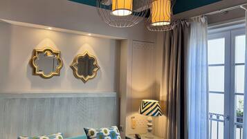 A bedroom with a bed, two wall mirrors, a nightstand with a lamp, and a window with curtains.