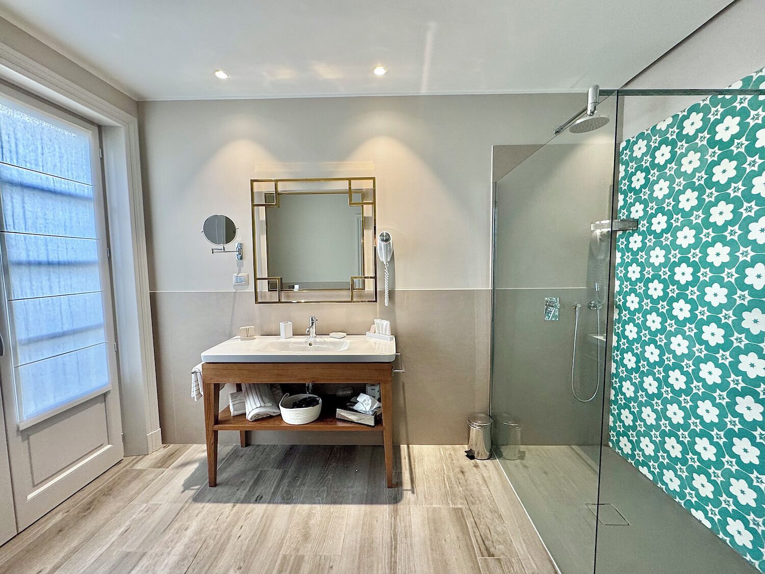 Un baño moderno con tocador de madera, un espejo grande, cabina de ducha de vidrio y pared con diseño.