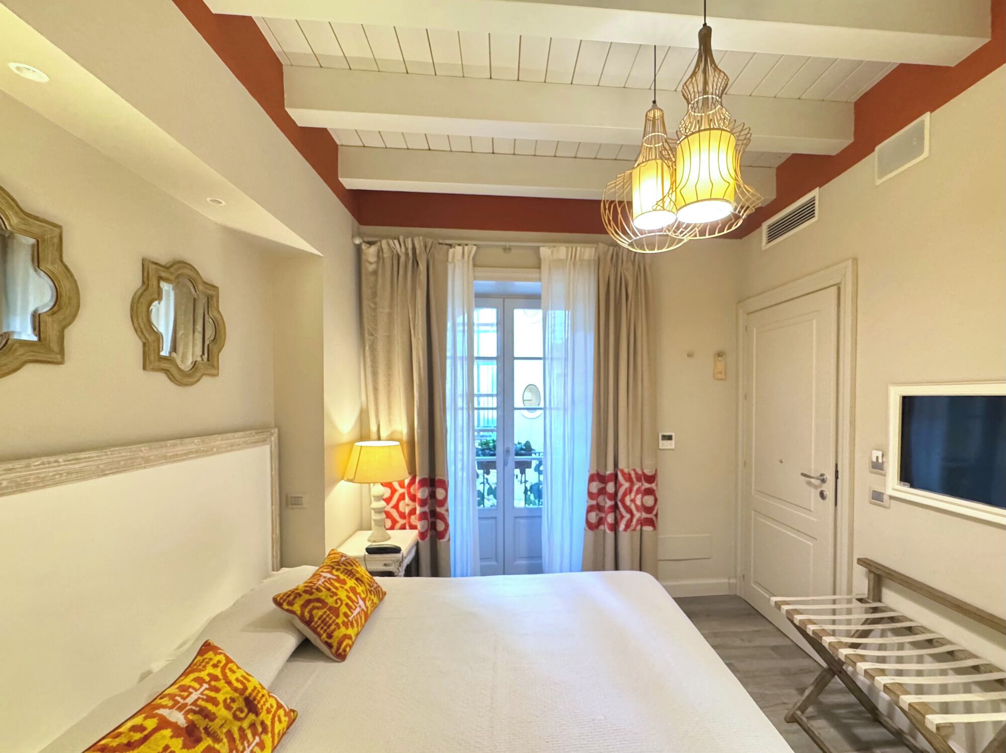A hotel room with a bed, a TV, a lamp, and a window with curtains.