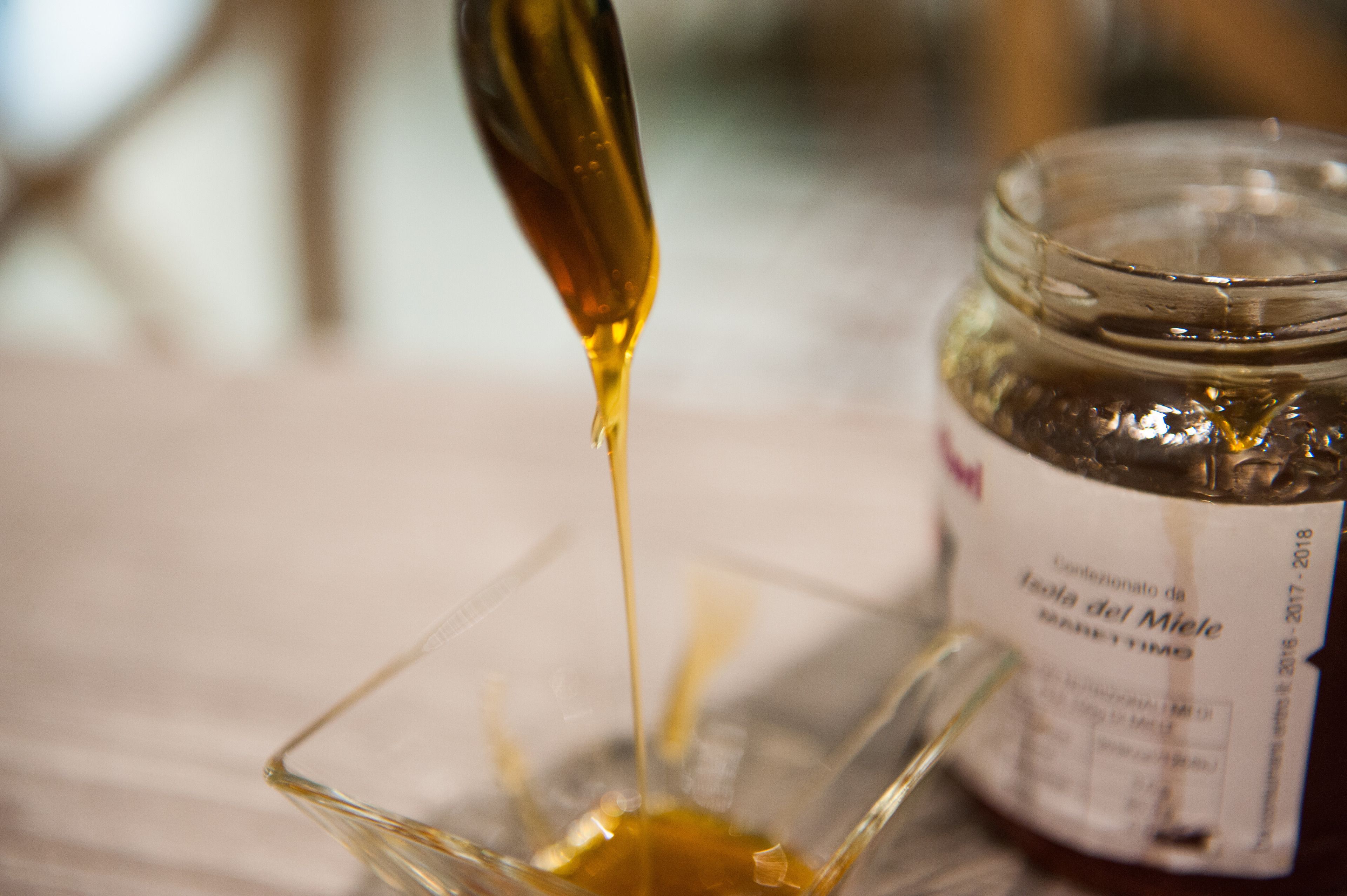 A glass container with a label and a spoon pouring a liquid into it.