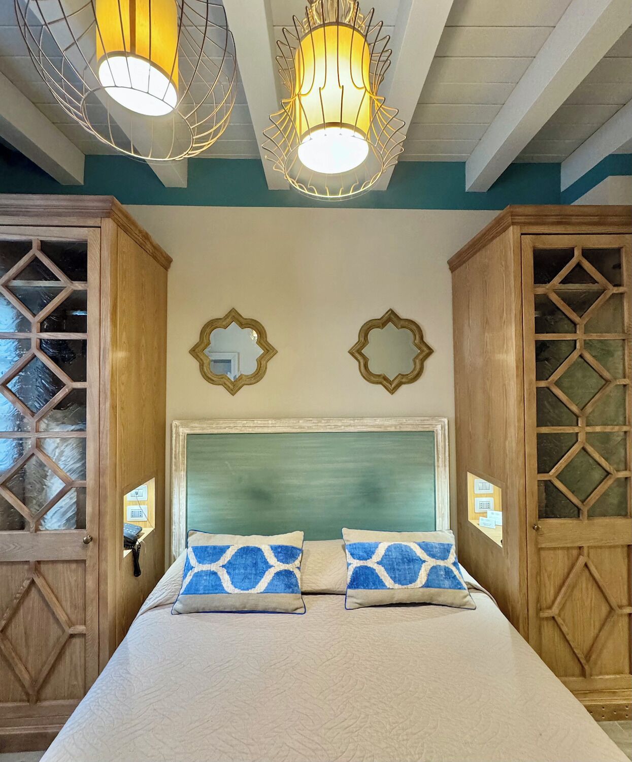 Un dormitorio con una cama grande, armarios de madera y dos espejos fijos a la pared.