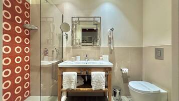 Un baño moderno con cabina de ducha de vidrio, tocador de madera con dos toallas, inodoro blanco y espejo sobre el lavabo.