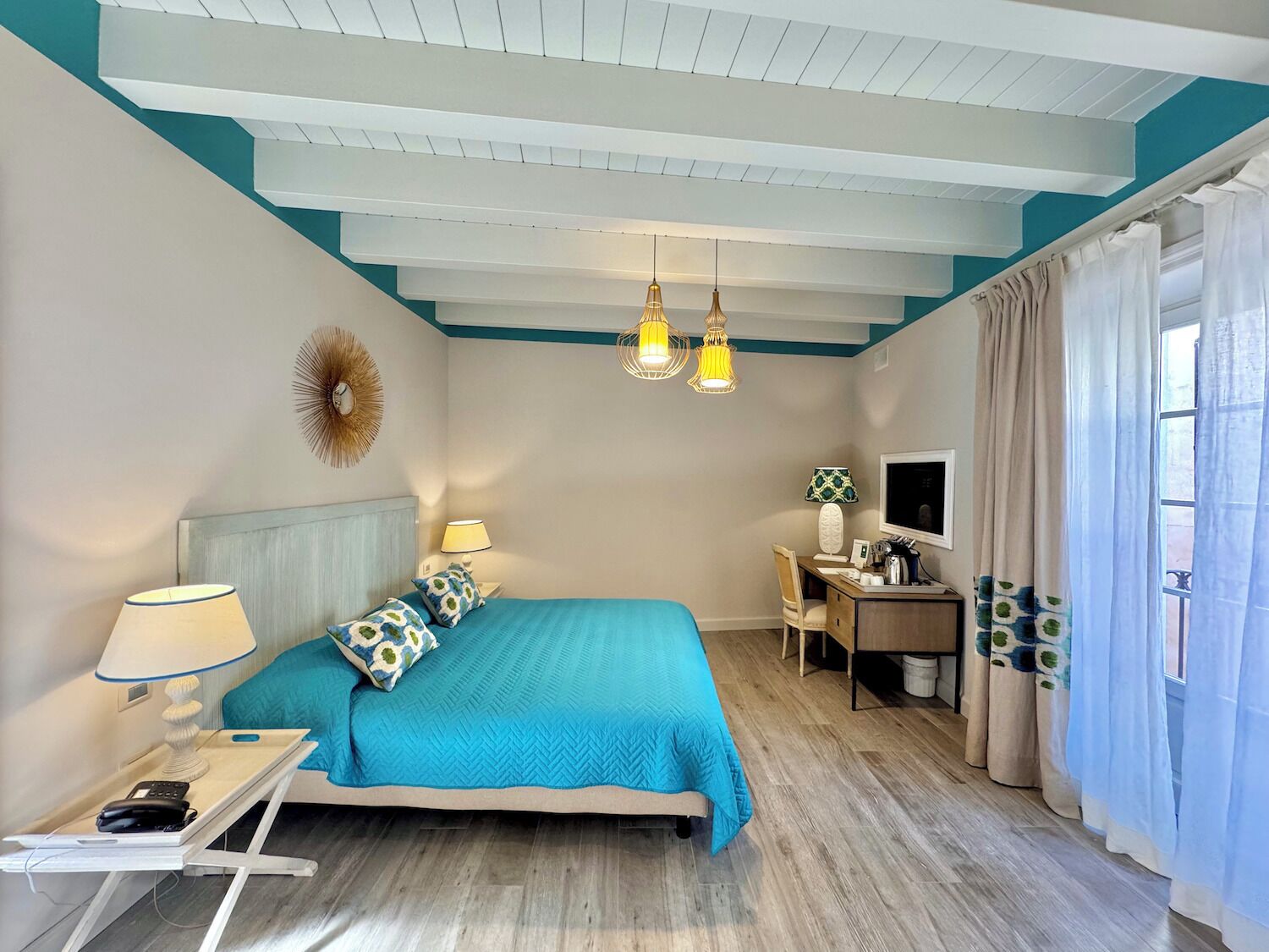 Una habitación de hotel con cama, mesita de noche, lámpara, escritorio, silla, televisor y cortinas.