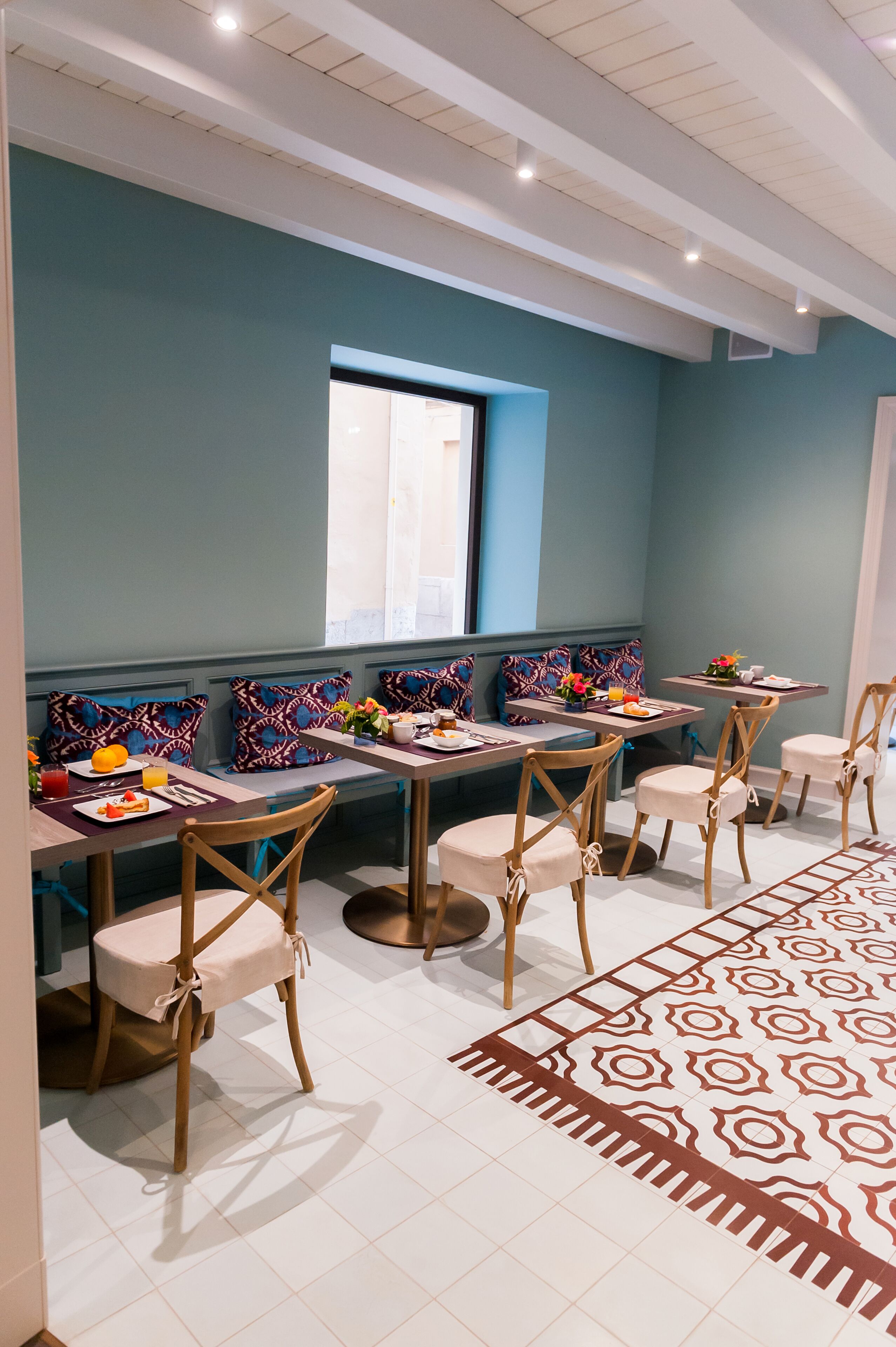Zona pranzo con tavoli e sedie, un tappeto decorato e una finestra con persiane.