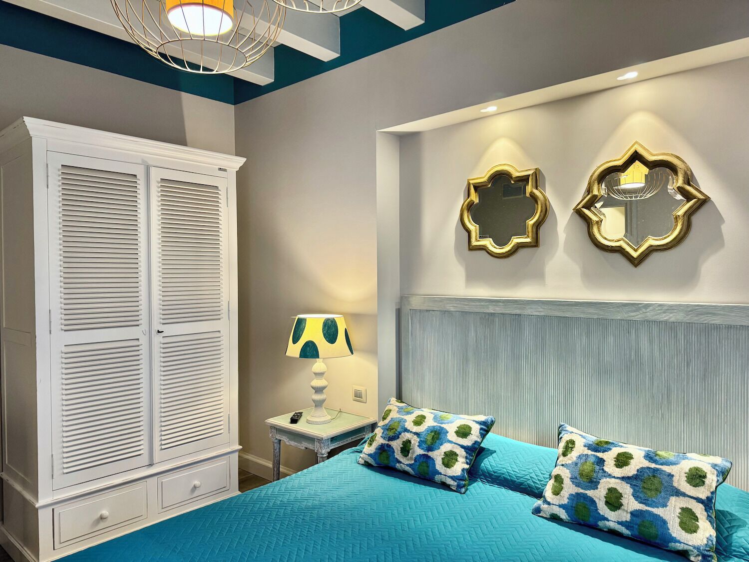 A bedroom with a bed, two wall mirrors, a bedside table with a lamp, and a wardrobe.