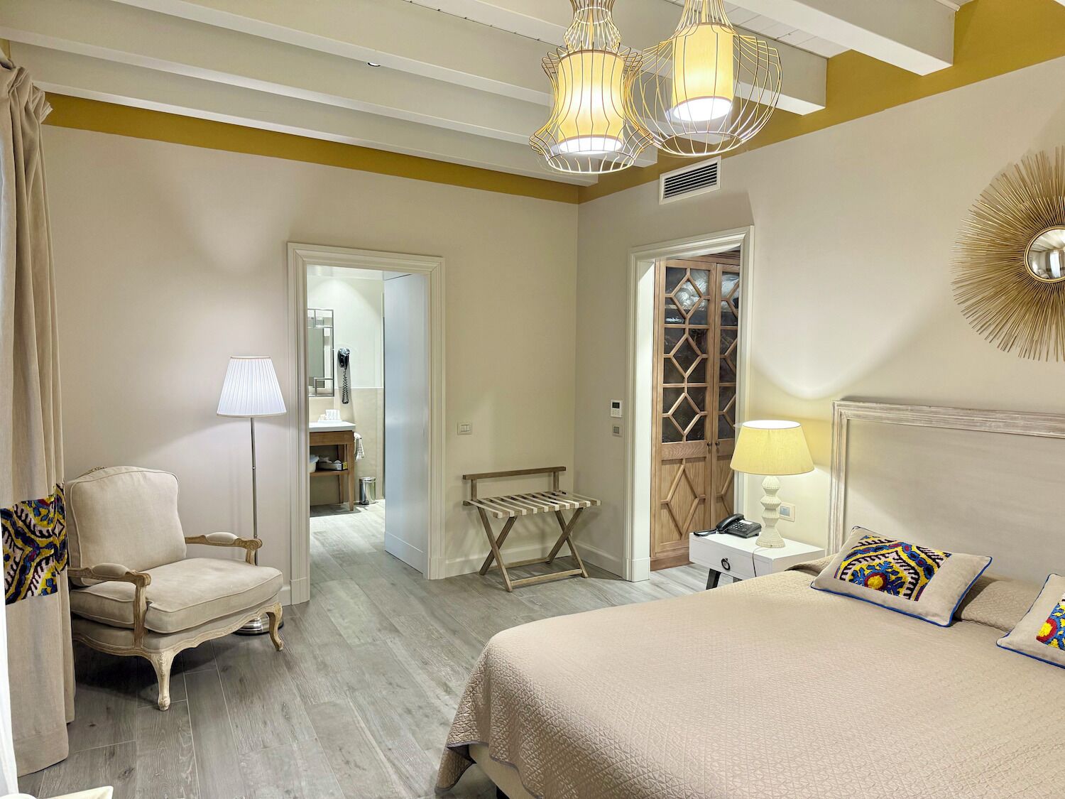 A hotel room with a bed, a chair, a lamp, a bedside table, and a wardrobe.