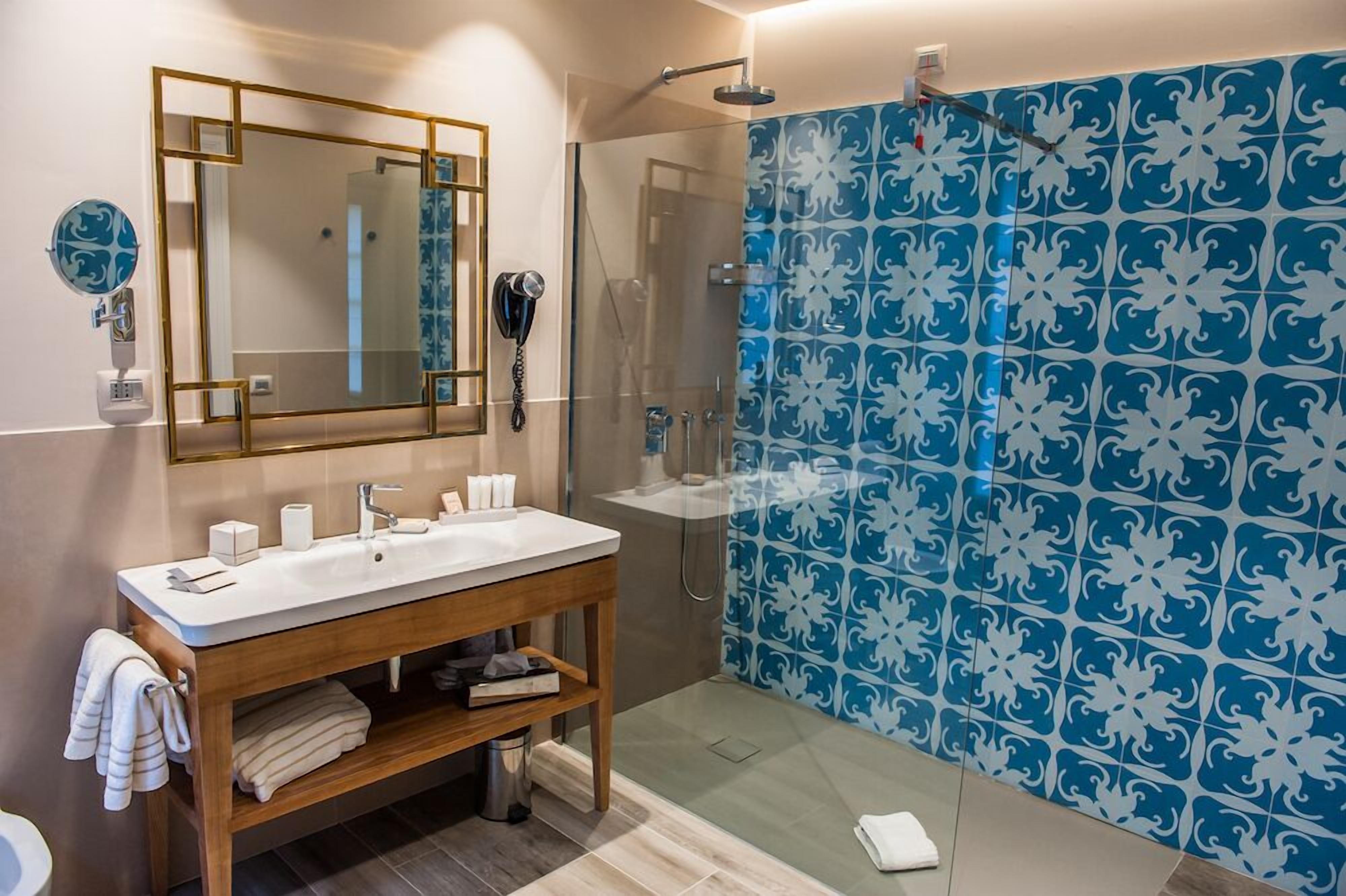 A bathroom with a wooden vanity, a large mirror, a shower, and blue patterned tiles.