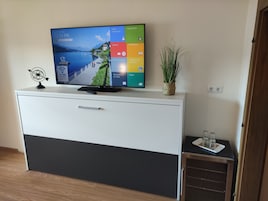 Un televisor de pantalla plana sobre un mueble blanco y negro, con un control remoto, un adorno pequeño y una planta en maceta.