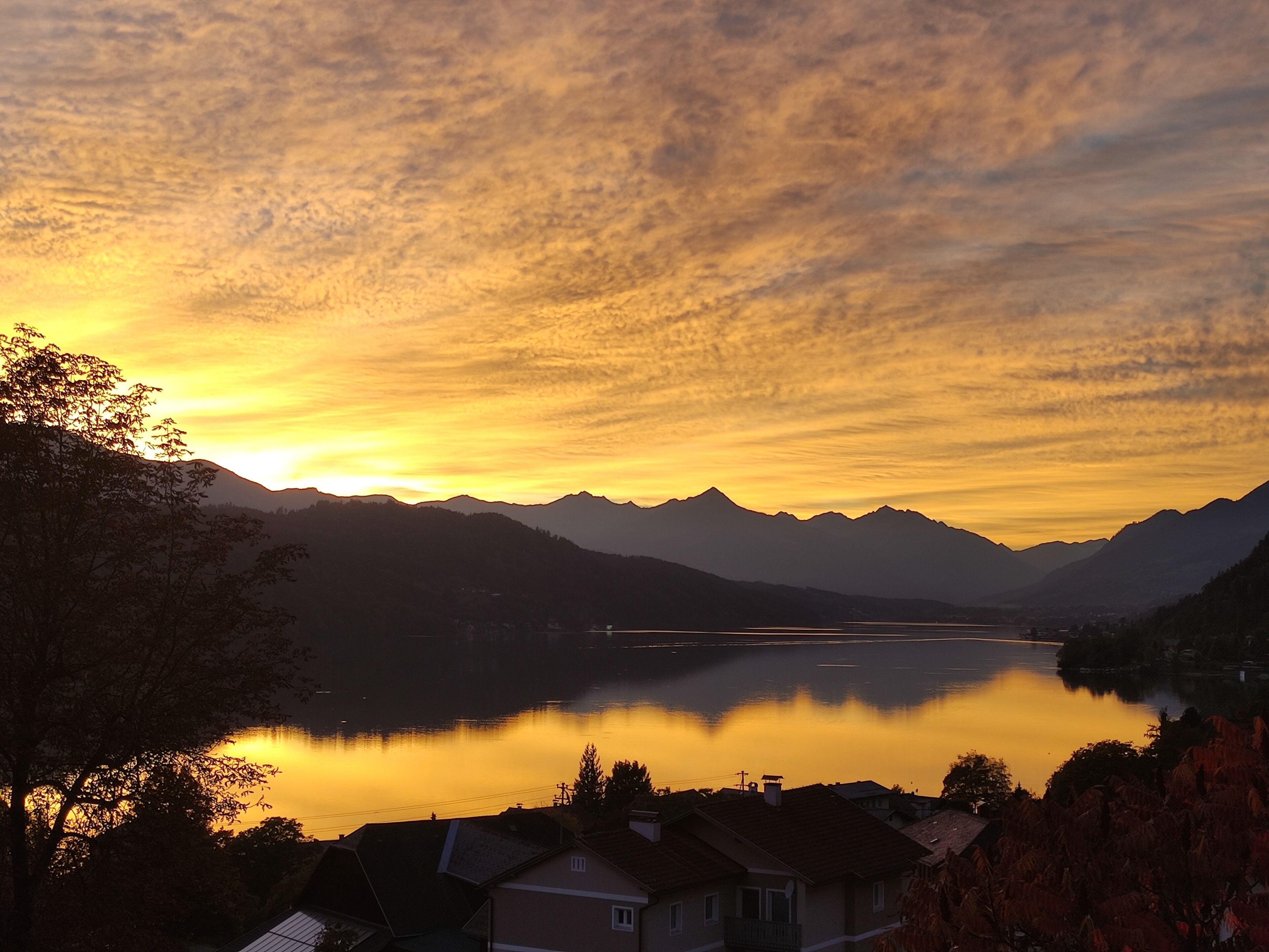 Ein See mit Bergen im Hintergrund und Häusern im Vordergrund.