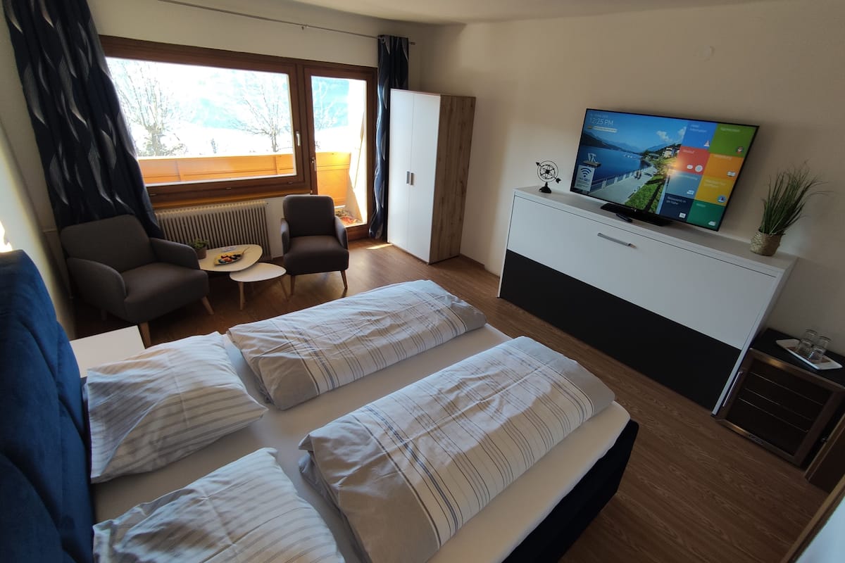 A hotel room with two beds, a desk, a chair, a TV, and a window with curtains.
