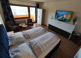 Habitación de hotel con dos camas, un escritorio, una silla, un televisor y una ventana con cortinas.