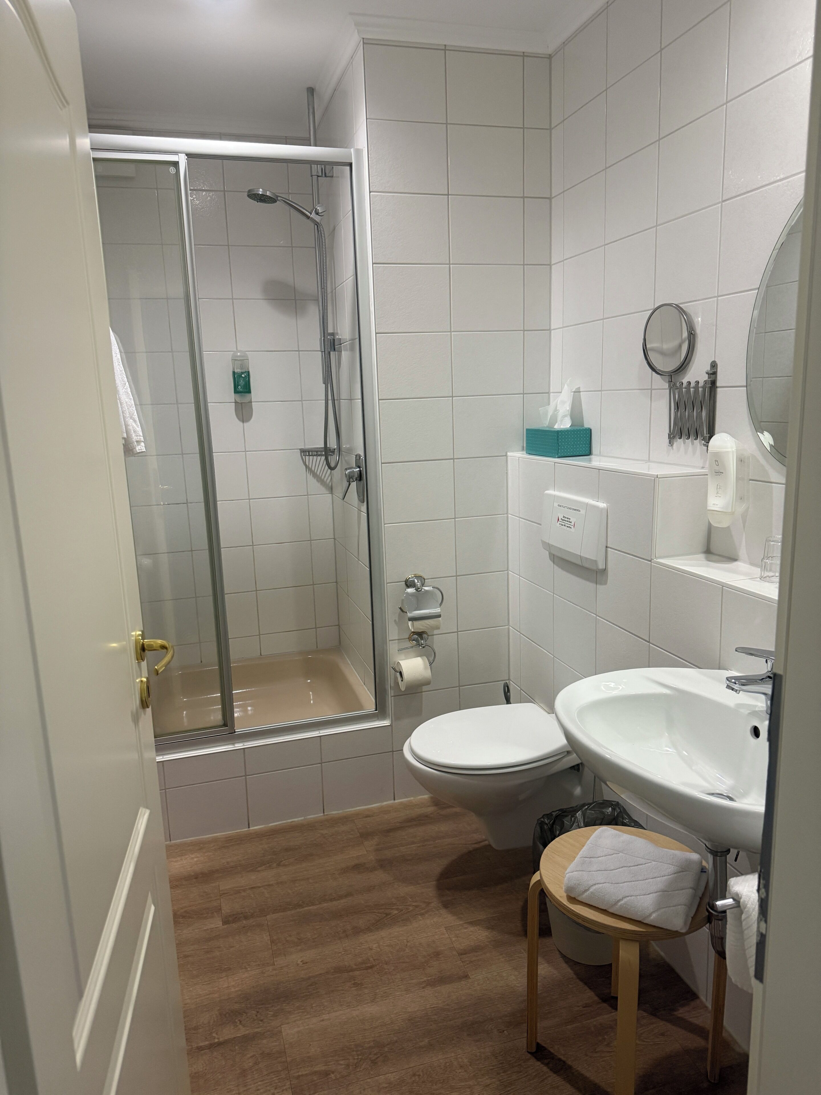 A bathroom with a shower, toilet, sink, and a small stool.