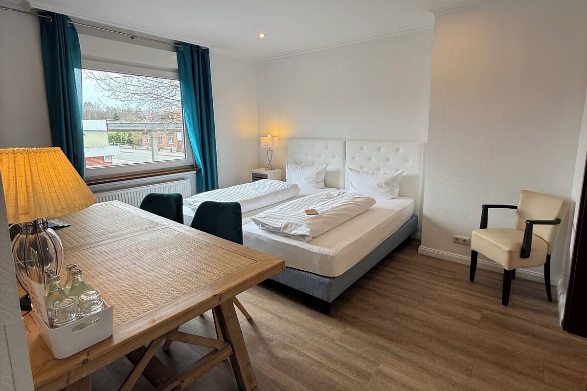 A hotel room with a bed, a desk with a lamp, a chair, and a view of the outside.