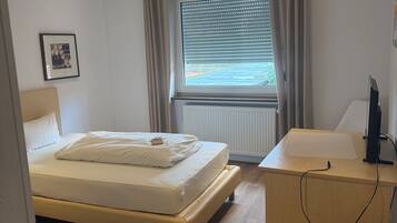 A bedroom with a bed, a desk, a chair, a window with curtains, and a radiator.