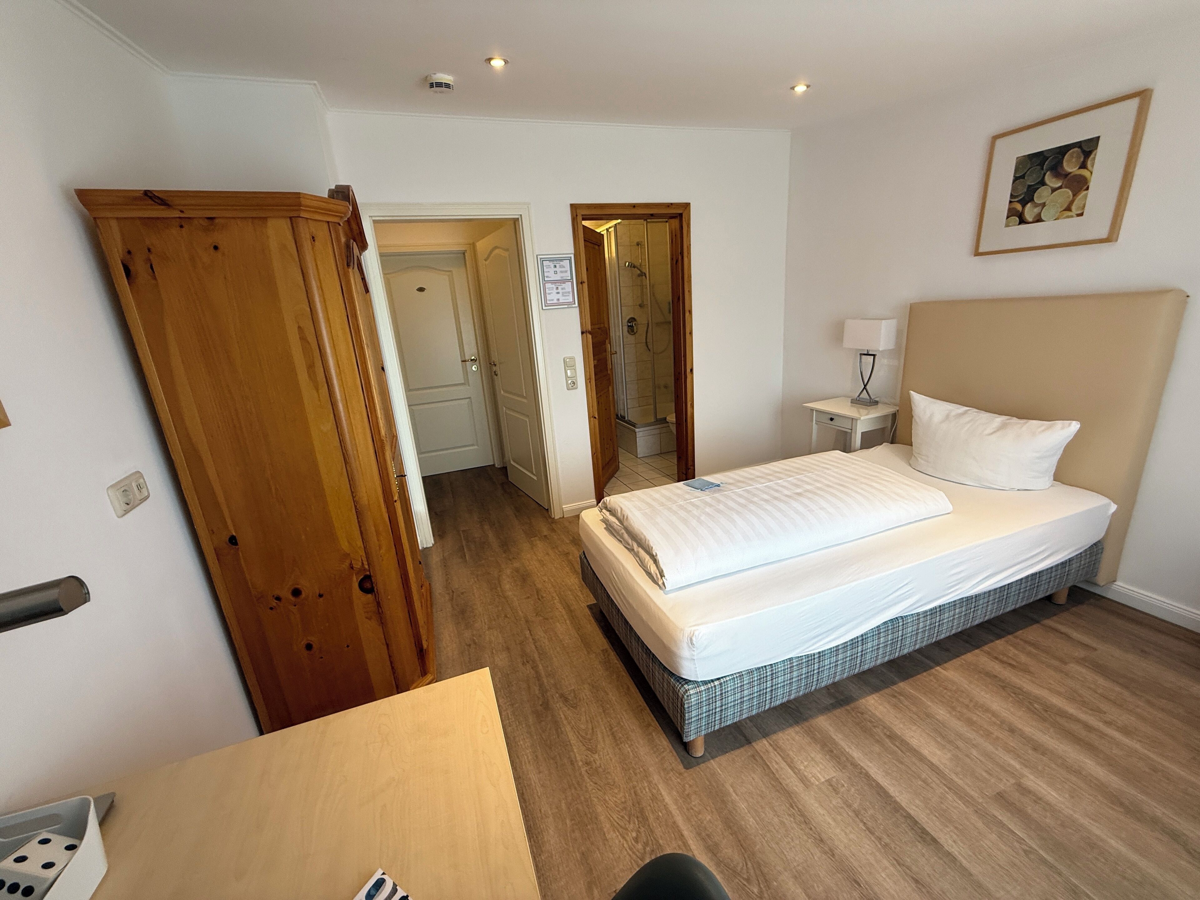 Ein Hotelzimmer mit Bett, Schreibtisch, Stuhl, Kleiderschrank und Duschbereich.
