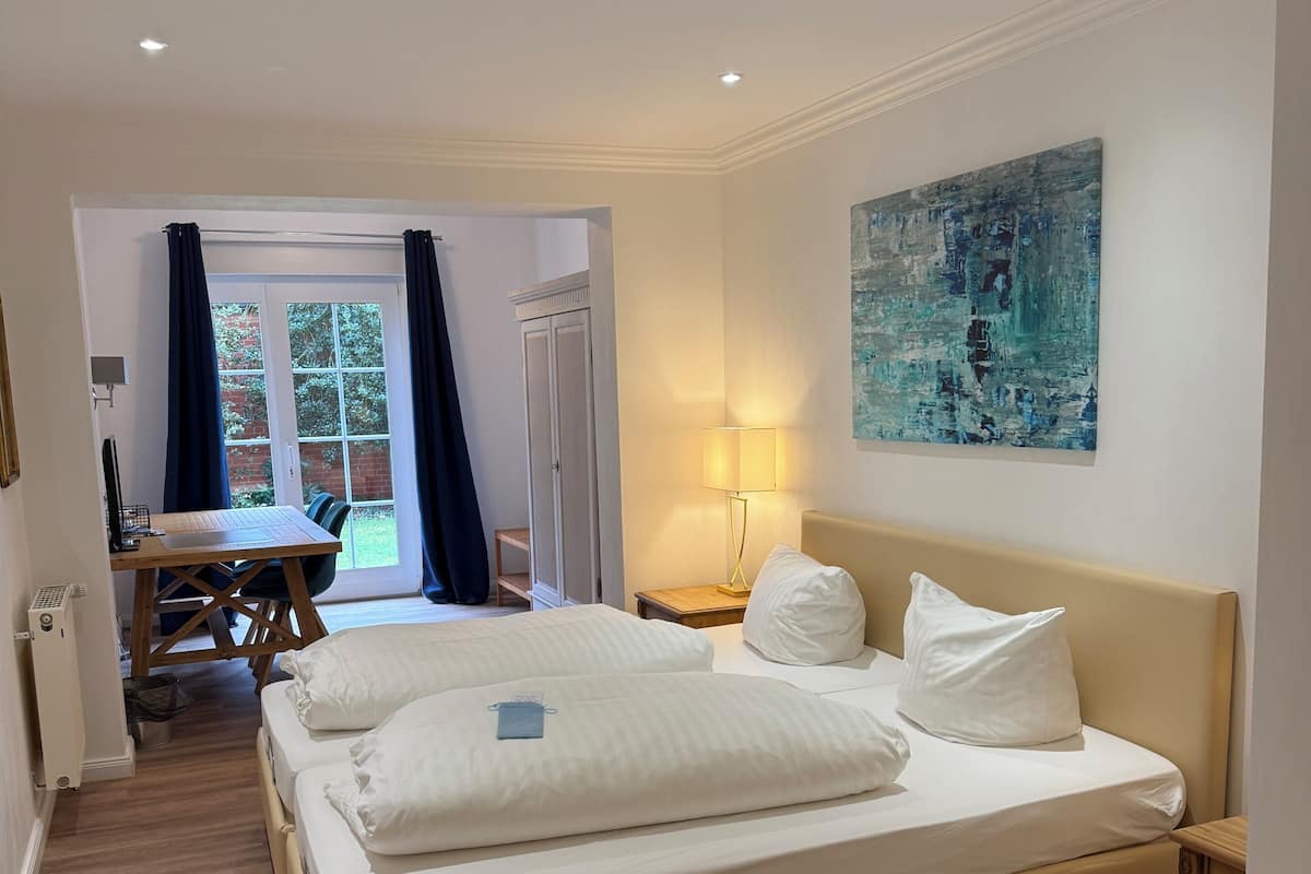 A hotel room with a large bed, a desk, and a chair, a window with curtains, and a painting on the wall.