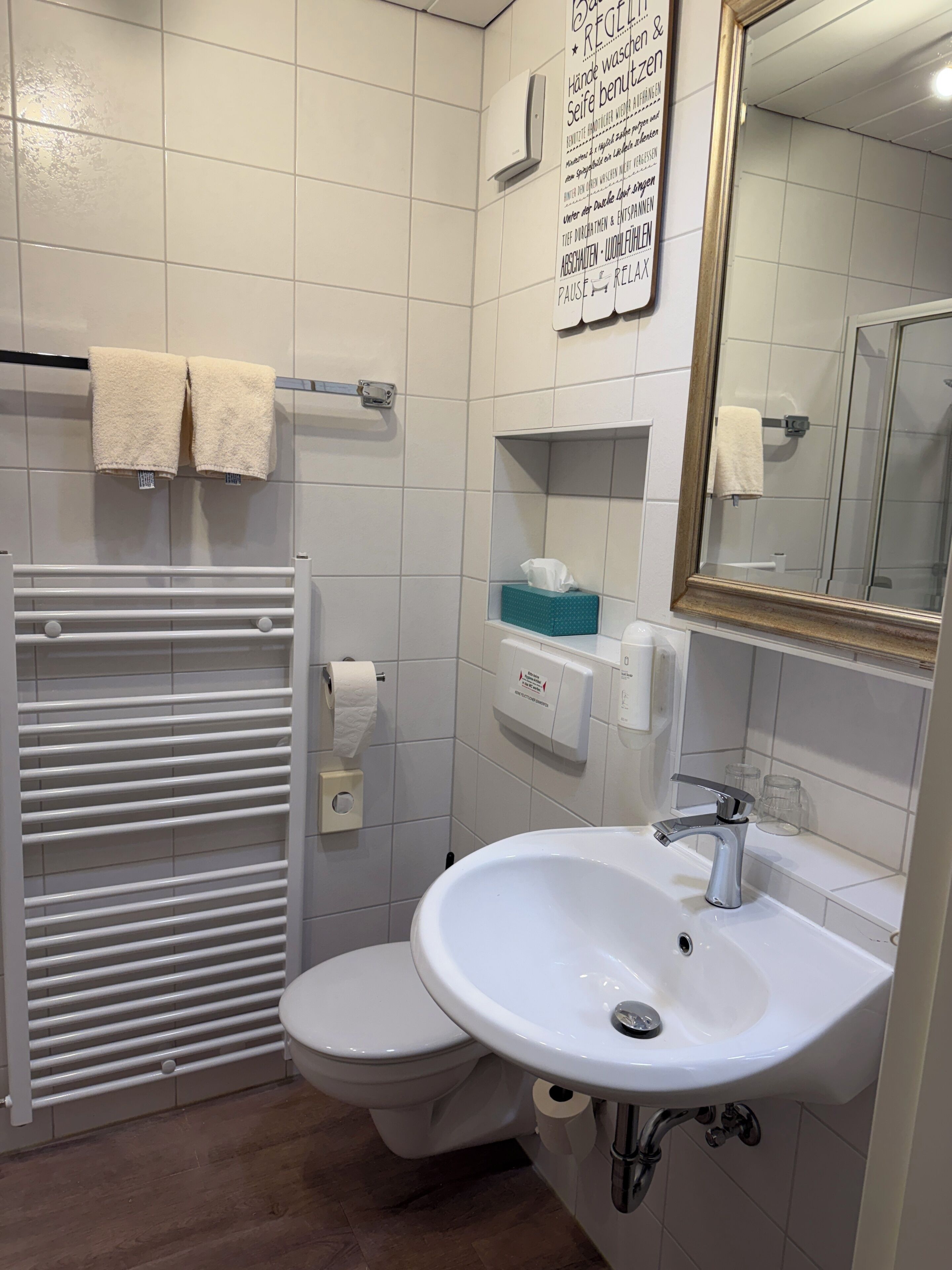 A bathroom with a toilet, a sink, a towel rack, a mirror, and a wall-mounted air purifier.